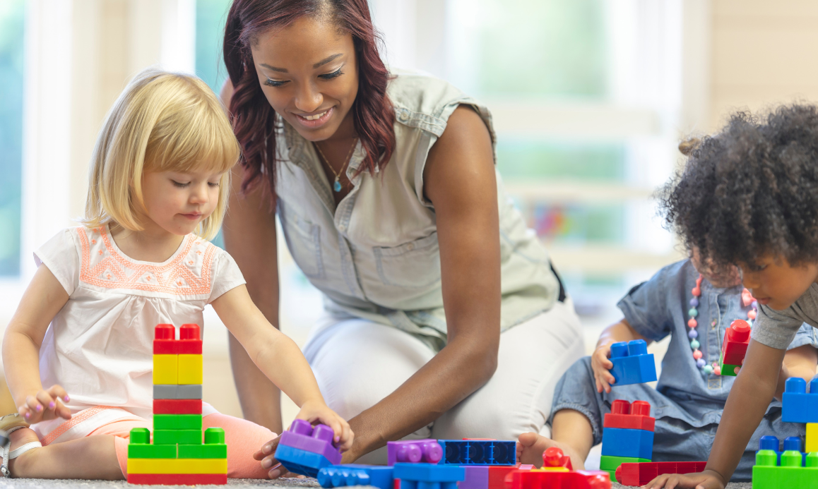 An early childhood educator plays blocks with some students