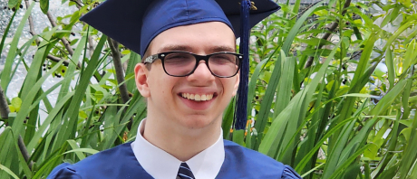 Close up picture of a boy smiling with a blue graduation cap and gown