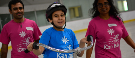 Boy riding bike with two adult workers following closely behind