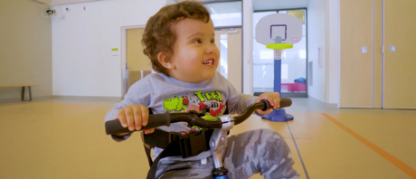 Young boy riding an adapted tricycle smiling. 