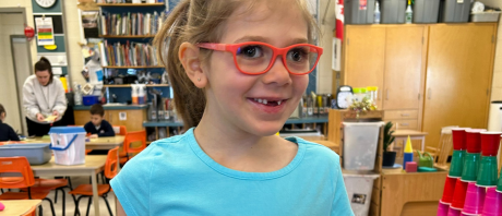Mikayla smiling, wearing red glasses and a blue tshirt.