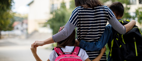 A mother with her arms around a daughter and a son wearing backpacks
