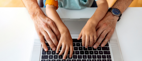 Aerial view of a child's hands on a keyboard with her hands being guided by her fathers hands.