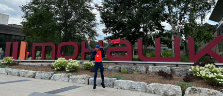 Jayden jumping for joy in front of the Mohawk College sign