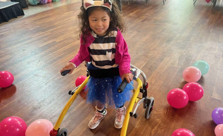 Audrey, a young Botox client, uses her walker to walk. She is surrounded by pink balloons.