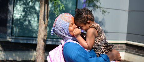 A mother embraces her daughter in a hug, picking her up and laying their foreheads against each other.