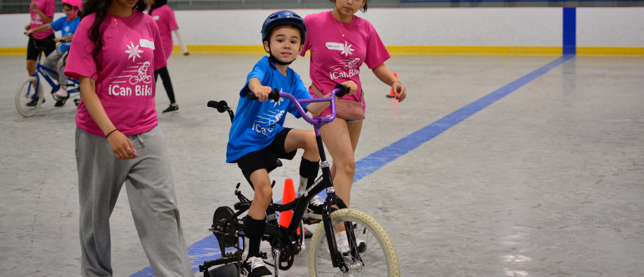 Two iCan Bike volunteers support a student on an adapted bicycle