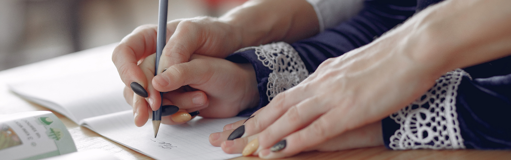 An adult uses hand over hand with a child to help with practicing writing