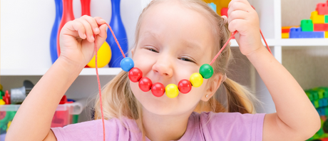 A child holds up a string of beads in front of her face like a smile.