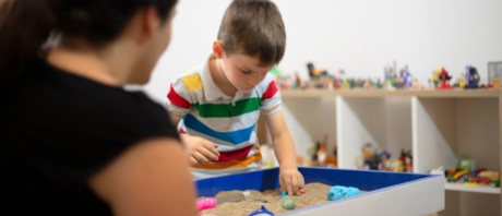 A child and therapist play with a sensory bin with sand.