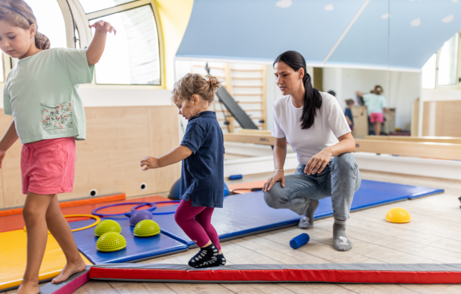 2 children walking on a balance beam with an occupational therapist supervising them.